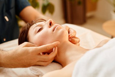 Güzeller güzeli genç bayanı kapayın ve SPA merkezinde yüz masajından zevk alın. Gözleri kapalı.