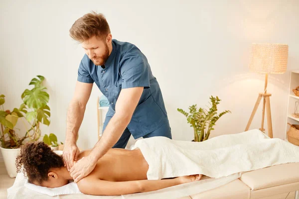 Portrait of male beautician giving back massage to young African American woman in SPA