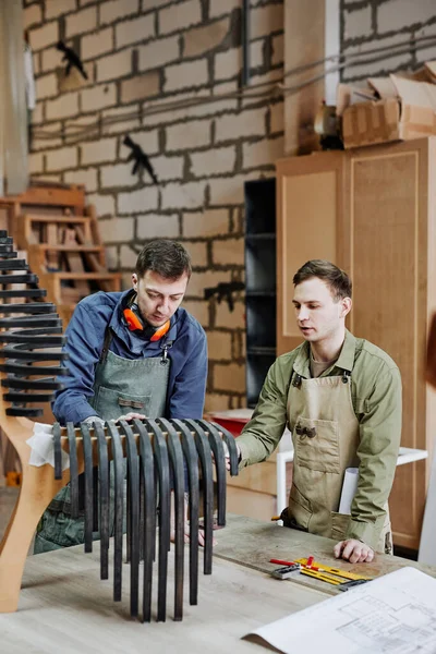 Vertical portrait of two carpenters working on handcrafted piece of furniture in workshop
