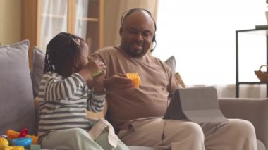 Afro-Amerikalı bir adam evde çalışırken dijital tablet kullanıyor. 3 yaşındaki güzel kızı yanında oturan oyuncaklarla oynuyor.