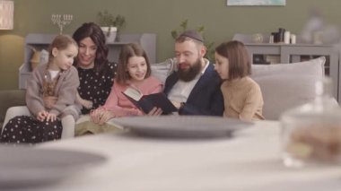 Beş kişilik mutlu Yahudi ailesi Hanuka 'yı evde kutlarken Tanakh' ı birlikte okuyorlar.