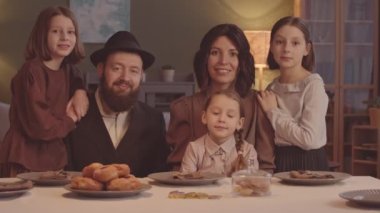 Hanuka 'da bayram yemeği yerken kameraya poz veren beş kişilik mutlu Yahudi aile portresi.
