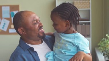 Mutlu Afrikalı Amerikalı adam göğsünde kucağında sevgili küçük kızı onu burnundan öpüyor ve gülümsüyor.
