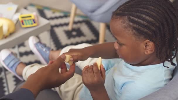 Nettes Afroamerikanisches Kleinkind Sitzt Auf Dem Sofa Und Isst Apfelscheiben — Stockvideo