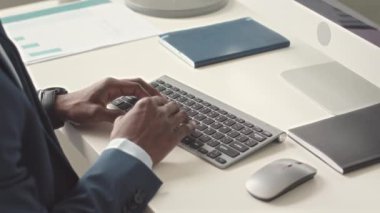 Ofisteki bilgisayarda çalışırken kablosuz klavyede yazan, zarif mavi takım elbiseli, tanınmayan siyahi adam.