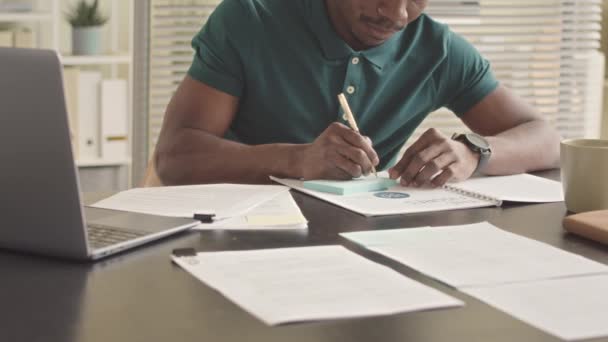 Cultivado Joven Negro Escribiendo Nota Adhesiva Mientras Hace Papeleo Sentado — Vídeo de stock