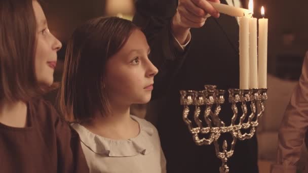 自宅でハヌカのお祝いの間 父親がケナカのろうそくを灯しているのを見ている小さなユダヤ人の少女たち — ストック動画