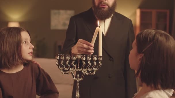 在光明节和他的两个小女儿在观看的时候 一个头戴帽子 蓄着大胡子的犹太男人慢慢地关上了灯 — 图库视频影像
