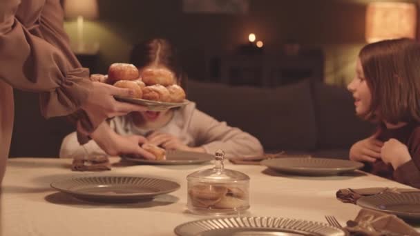 在光明节期间 一个默默无闻的女人坐在节日餐桌前 给她的小女儿们端上被称为 Sufganiyot 的糊状甜甜圈 — 图库视频影像