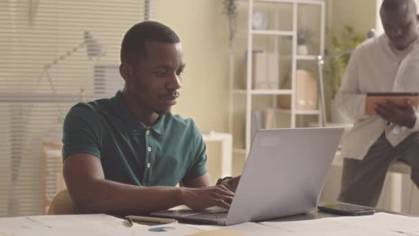 Νεαρός Μαύρος Πληκτρολογεί Φορητό Υπολογιστή Κάθεται Στο Γραφείο Ενώ Συνάδελφός — Αρχείο Βίντεο