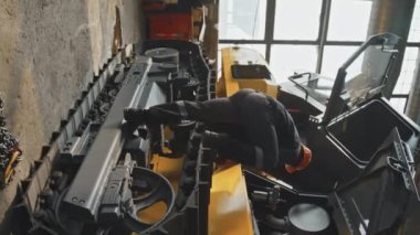 Siyahi erkek makine mühendisinin endüstriyel makine fabrikasında traktör tamir ederken dikey çekimi.
