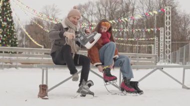 Neşeli genç beyaz çift kış tatillerinde buz pateni yapmaya hazırlanırken arka planda güzel dekore edilmiş Noel ağacıyla buz pateni yapıyor.