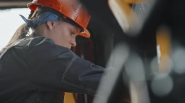 Endüstriyel fabrikadaki buldozer makinesini tamir etmek için özel krank anahtarı kullanarak kadın tamircinin yavaş yavaş inmesini sağlayın.