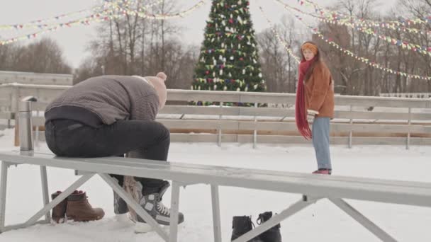 一对浪漫的年轻夫妇在户外冰场约会 背景是装饰精美的圣诞树照明 — 图库视频影像