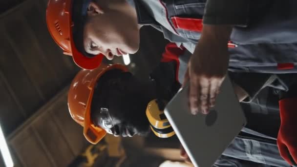 机械设备制造厂内讨论的两个戴着橙色硬礼帽的男女工程师的竖直低角度 — 图库视频影像