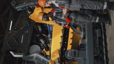 İki farklı mühendisin sabit şapka ve tulum giyip sanayi bölgesinde buldozer başında dikey çekimleri tartışmaları.