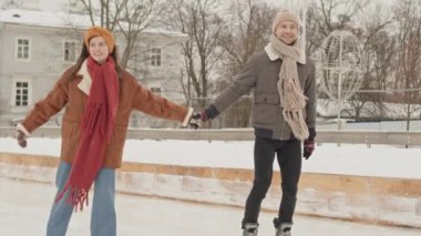 Romantik genç beyaz çift, buz pateni pistinde el ele tutuşup sohbet ediyorlar.