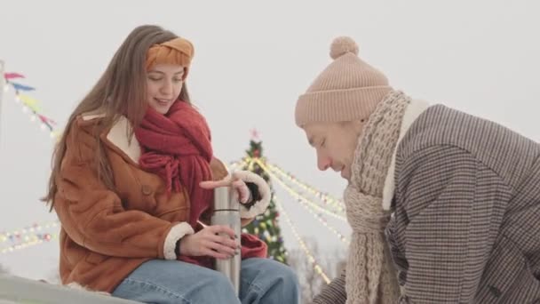 年轻的白人男子帮助他的女朋友们把鞋带绑在溜冰鞋上 在户外冰场举行浪漫的约会 — 图库视频影像