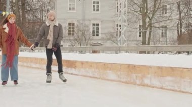 Sıcak kış giysileri içinde genç beyaz çift buz pateni pistinde el ele tutuşurken sohbet ediyorlar.