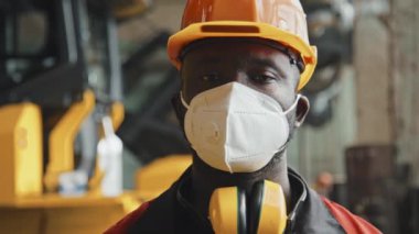 İş yerinde kameraya poz veren siyah erkek traktör fabrika işçisinin orta boy yakın plan portresi.