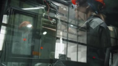 Kafkasyalı kadın elektrikçi turuncu şapka ve güvenlik gözlüğü takıyor ve makine ekipmanlarına kablo bağlıyor.