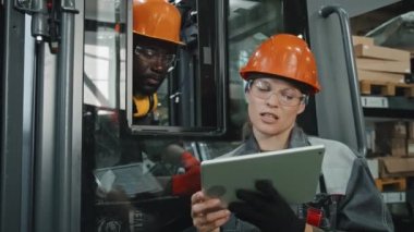 Tablet bilgisayarlı kadın mühendis, fabrikada traktör tamir ederken Afrikalı Amerikalı erkek meslektaşlarıyla konuşuyor.