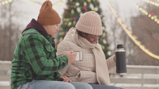 Młode Wielonarodowe Lesbijskie Dziewczyny Randce Lodowisku Pijąc Herbatę Termosu Siedząc — Wideo stockowe