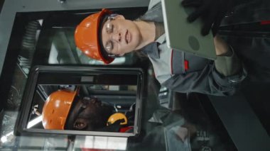 Fabrikadaki endüstriyel makine ekipmanlarını tamir ederken iş arkadaşıyla konuşurken tablet bilgisayarına bakan kadın mühendis.