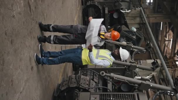 2人の多様な男性と女性エンジニアが工業工場で印刷された図面スキームを調べた垂直撮影 — ストック動画