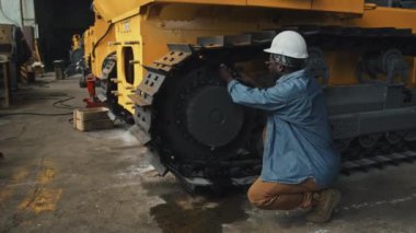 Profesyonel Afro-Amerikan erkek tamirci fabrika üretim makineleri ve araçlarda tekerlek yükleyicisini tamir ediyor