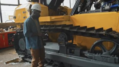 Afrikalı Amerikalı erkek servis teknisyeni fabrikadaki traktör makinesini tamir etmek için İngiliz anahtarı kullanıyor.