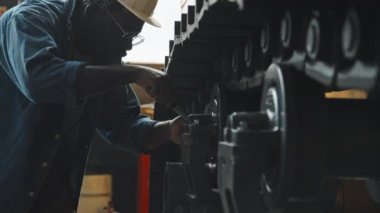 Kapalı alanda traktör tamir ederken İngiliz anahtarı kullanan kot gömlekli ve kasklı siyah erkek servis teknisyeni.
