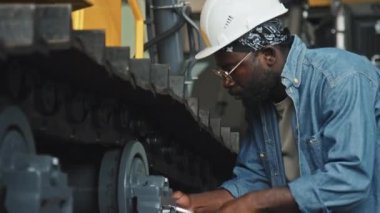 Genç siyahi adam traktör fabrikasında tamirci ya da servis teknisyeni olarak çalışıyor.