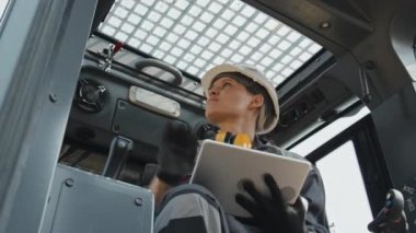 Profesyonel kadın mühendis, traktör kabinini kontrol edip inceleyerek tablet bilgisayara not alıyor.