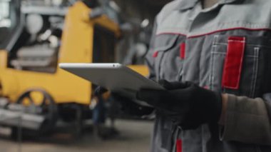 Tesis üreticisi traktörler ve diğer makinelerde çalışırken, eldiven ve kapsama alanındaki tanınamayan teknisyenlerin görüntüsü tablet bilgisayarında.
