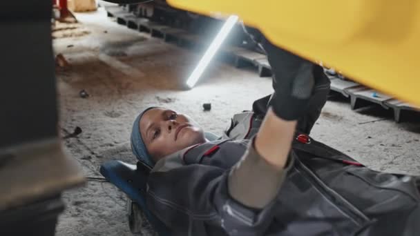 专业的女拖拉机机修工 躺着和在机器下工作时使用螺栓扳手 — 图库视频影像