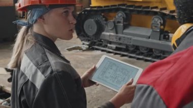 İki profesyonel traktör mühendisi, üretim tesisinde birlikte çalışırken tablet bilgisayarda aracın şemasını tartışıyorlar.