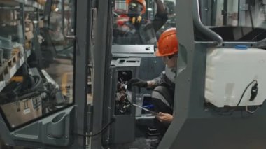 Çok ırklı teknisyenler traktör kabininde elektriği inceliyor, makine üretim tesisinde birlikte çalışıyorlar.