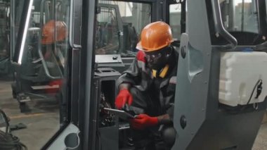 Siyah şapkalı Afrikalı Amerikalı adam traktör kabinine elektrik kurarken dijital tablet kullanıyor.
