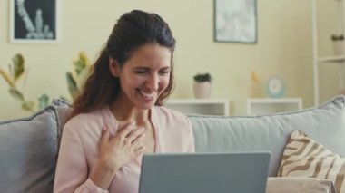 Memleketten bir arkadaşıyla çevrimiçi video görüşmesi yaparken dizüstü bilgisayara el sallayan ve gülümseyen neşeli beyaz bir kadın.