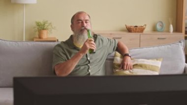 Heyecanlı, beyaz, gri sakallı, kanepede oturup bira içen ve evde TV 'de maç izleyen son sınıf öğrencisi.
