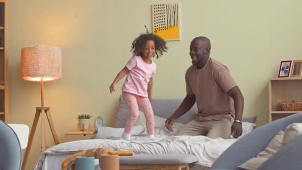 快乐的黑人男人和他漂亮的3岁女儿在床上玩耍 — 图库视频影像