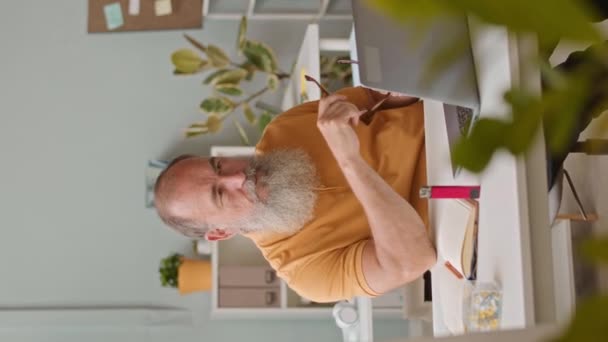 Pionowe Ujęcie Brodatego Starszego Mężczyzny Palącego Papierosa Elektronicznego Podczas Pracy — Wideo stockowe