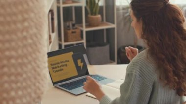 Evden smm trendleri üzerinde çalışan genç bayan pazarlama uzmanı, dizüstü bilgisayardaki slayt sunumunu analiz ediyor