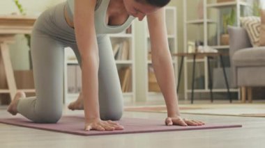 Genç ve rahat bir kadın, gündüz vakti sakin bir evde yoga yaparken minderde poz veriyor.