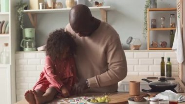 Afro-Amerikan babası ve 3 yaşındaki güzel kızı ahşap mutfak masasında manyetik alfabe harfleriyle oynuyorlar.