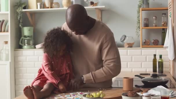アフリカ系アメリカ人の父親と彼の可愛い3歳の娘は木製のキッチンテーブルで磁気アルファベットの文字で遊んでいます — ストック動画