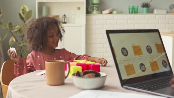 美国黑人小女孩玩教育玩具 而她的父亲则在电脑上工作 白天一起坐在厨房桌旁 — 图库视频影像