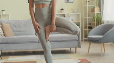 Genç, zayıf bir kadının tek bacaklı yoga pozunu dengede tutarken, evde tek başına yoga yaparken.