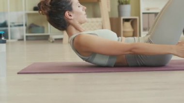 Dar giysili genç bir kadın gündüz antrenman yaparken minder üzerinde karın egzersizi yapıyor.